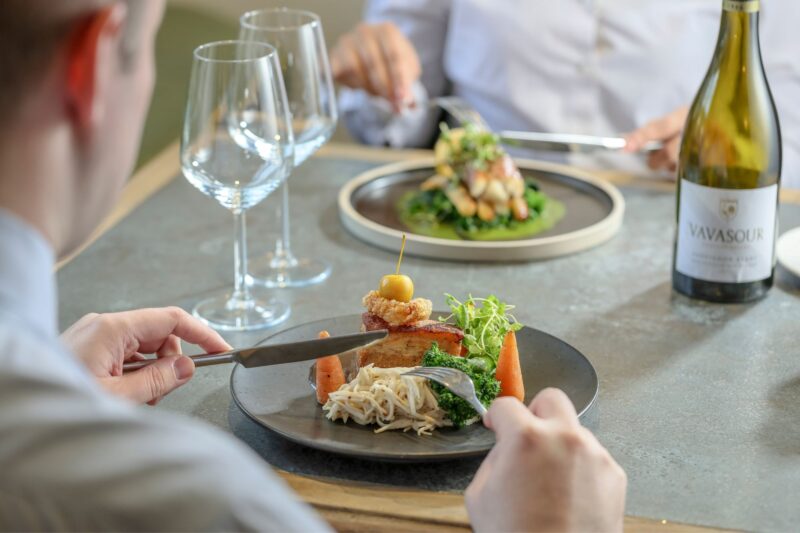 Couple eating with crispy pork belly being cut into and monkfish tail wrapped with Serrano ham